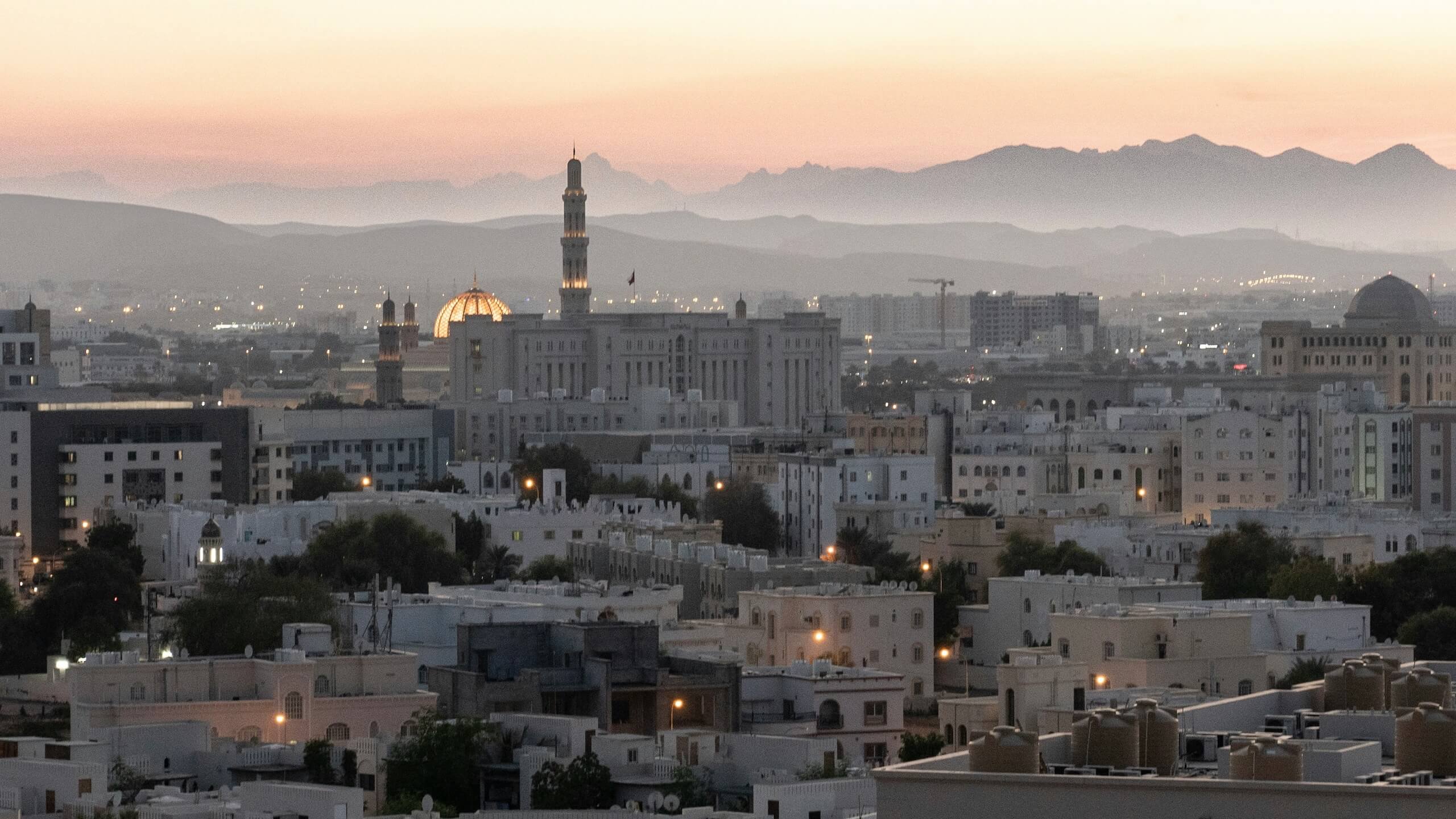 Dusk over Muscat, Oman’s capital, where mountains, sea, and city converge. Positioned on the southeastern edge of the Arabian Peninsula with access to the Indian Ocean and Arabian Sea, this geography anchors Muscat’s quiet but pivotal role in regional diplomacy and mediation.